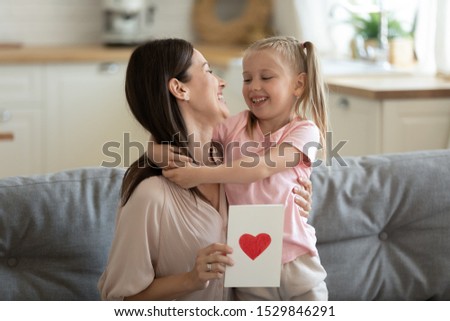Happy mother hugging little daughter, thanking for gift postcard, expressing love and gratitude, preschool girl presenting postcard to excited mum, family celebrating birthday or women mothers day