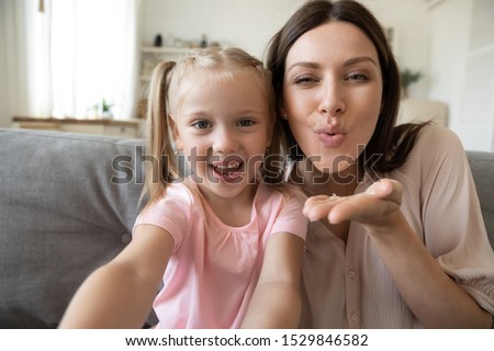 Head shot happy little daughter and mother taking selfie, sending blow kiss close up, having fun, loving smiling mum and adorable preschool child looking at camera, enjoying free time together