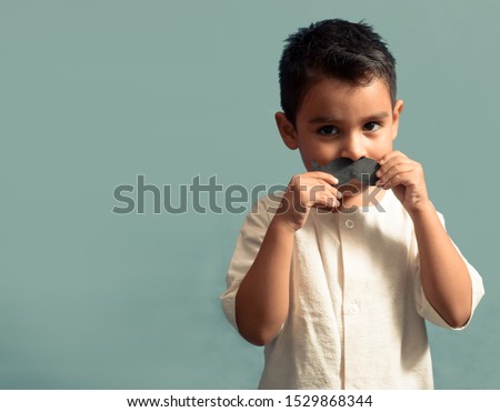 little kid joking with a fake paper moustache. Happy child playing in home. Isolated background. Movember concept. Royalty-Free Stock Photo #1529868344