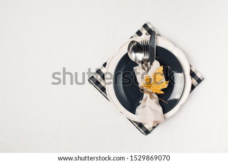 Autumn thansgiving and halloween tableware flat lay with plate and golden leaves on white cloth background, copy space, top view