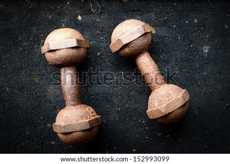 a pair of vintage iron rusty dumbbells on dirty black background 