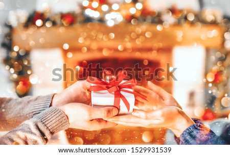 Christmas Gift in hands. Happy Man giving Christmas and New Year Gift box to woman at Home. Family Xmas celebration. Person Holding, Receiving a Gift box. Christmas decoration. Relationship