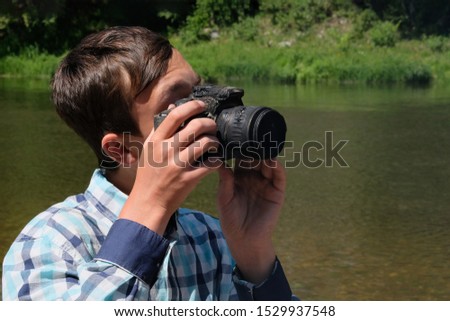 Heat or the effects of fire. The camera melted in the hands of a teenager. A strange situation in nature. A guy in a plaid shirt looks through the peephole of the DSLR. Taking pictures with a burned