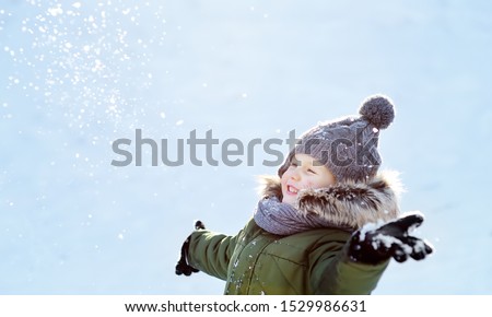 Little boy is having fun playing with snow. Kid dressed in a warm clothes, hat, hand gloves and scarf. Active outdoors leisure with children in winter.
