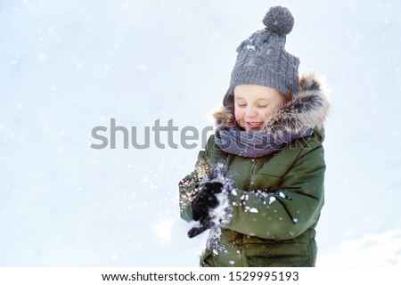 Little boy is having fun playing with snow. Kid dressed in a warm clothes, hat, hand gloves and scarf. Active outdoors leisure with children in winter.