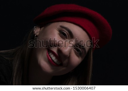 Portrait of young woman with red hat in studio with black background.