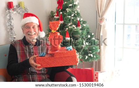 Happy people holding Christmas presents. Christmas tree on background. Senior man with beard and Santa's cap