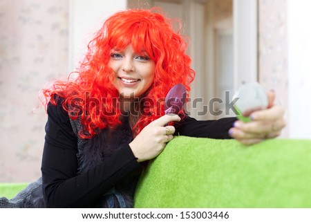 Woman in red wig looks to mirror at home
