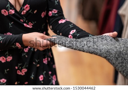 Quality photo of the fabric of a gray sweater, which is carefully probed by a young girl. Fabric quality. Sale. Clothing. Black Friday. Choice. Close-up.