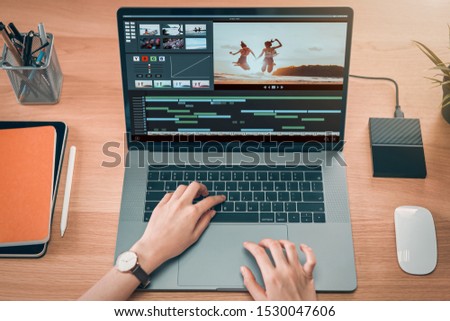 Concept of simple operation of blogger and vlogger, hand using laptop on video editor works with footage on wooden table, camera and accessories on table.