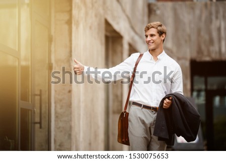 A young handsome businessman happily catches a taxi after leaving the office