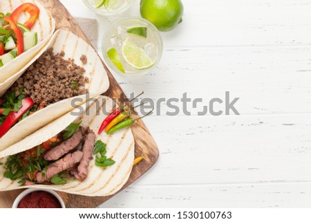 Set of mexican tacos with meat and vegetables in tortilla. And caipirinha cocktail. Top view on wooden table. Flat lay with copy space