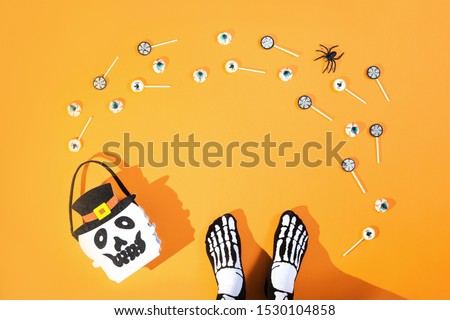 Happy Halloween candy bucket face of Jack O Lantern with lollypops with spiders and nets on orange background and bloody eyes sweets and sceleton feet. Flat lay trick or treat banner with copy space