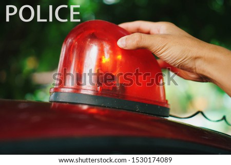 The hand is holding the fire red siren flasher. Siren on police car flashing, close-up.