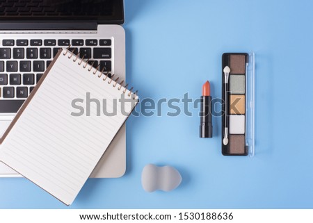 Top view of cosmetics and laptop on blue background
