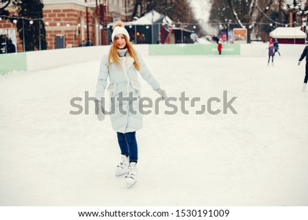 Girl in a winter park. Beautiful lady in a blue jacket. Woman in a ice arena