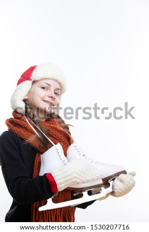 Winter Activities Concepts.Happy Caucasian Girl With Pigtails Posing in Winter Outfit With Ice-Skates Against White in Studio. Vertical image