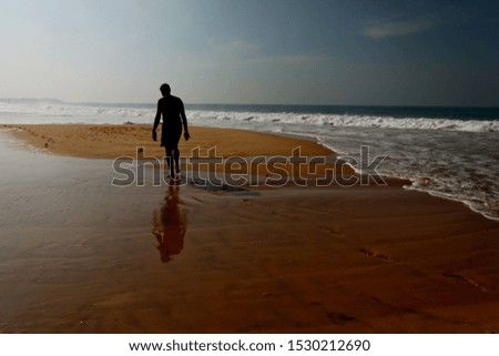 A horizontal shot of a man's silhouette walking on a beach near a body of water with beautiful waves
