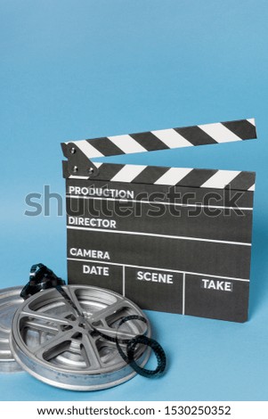 Clapperboard with film reel and film stripes against blue backdrop