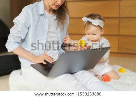 Little girl with mother watching cartoons online on laptop. Young woman entertaining daughter with funny videos for kids. Female trying to work, watch webinar, get distant education taking care of kid