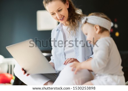 Smiling mom showing daughter funny pictures and photos on laptop. Early development programs for toddlers online. Baby girl watching cartoons on computer with mother. Digital tools, channels and tv.