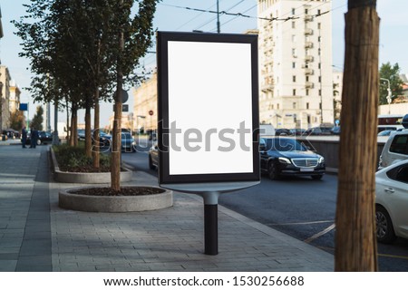 Digital billboard with blank screen for commercial advertising standing in busy street. Road with busy traffic, cars and public transport passing by. People walking along sidewalks, business buildings