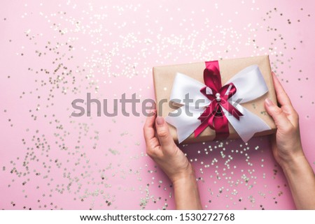 Gift or present box with a big bow in the hands of a woman on a pink table. Flatlay composition for Christmas birthday, mother day or wedding