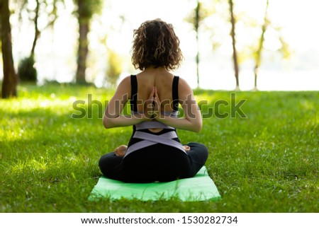 Beautiful smiling woman in morning park doing yoga and outdoor gymnastics. Green grass and rays of sun.