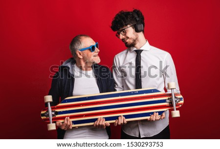 Young man and senior father with longboard in a studio on red background.