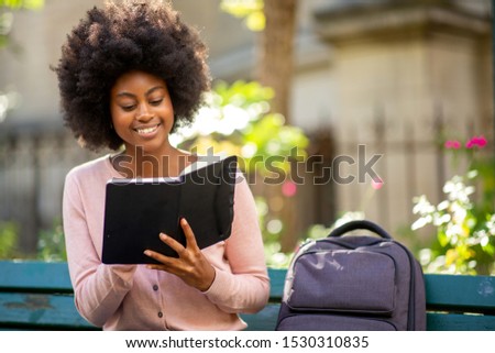 Portrait of young smiling african american woman reading book outside