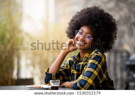 Portrait of young black woman with afro hair and glasses sitting outside and smiling