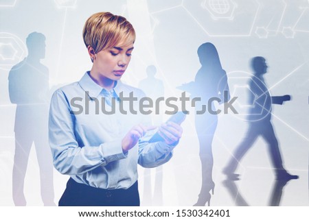 Serious young businesswoman using smartphone in blurry city with business people silhouettes in background and double exposure of digital interface. Concept of internet and hi tech. Toned image