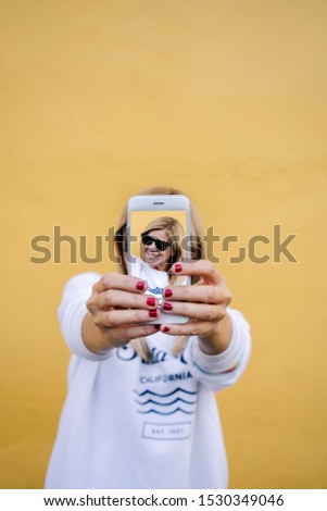 Beautiful caucasian blondie woman taking a photo with phone on a yellow wall