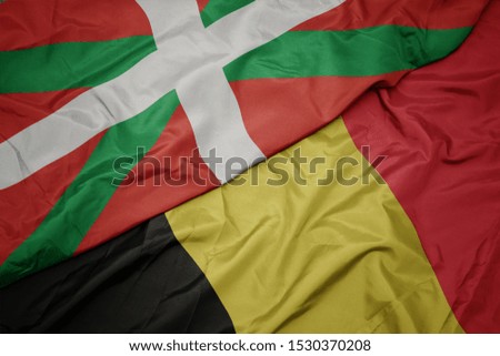 waving colorful flag of belgium and national flag of basque country. macro