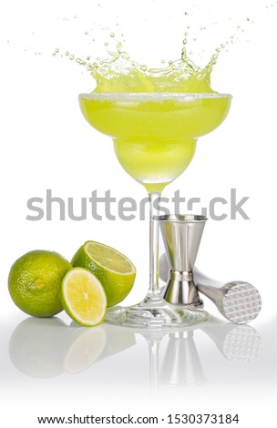 bartender tools and lime fruits around a splashing margarita glass