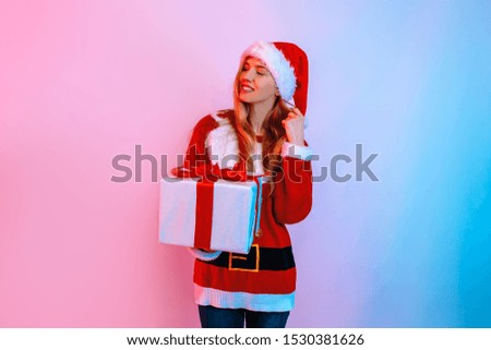 Happy thoughtful girl in Santa hat with Christmas gift standing on background with red and blue neon light