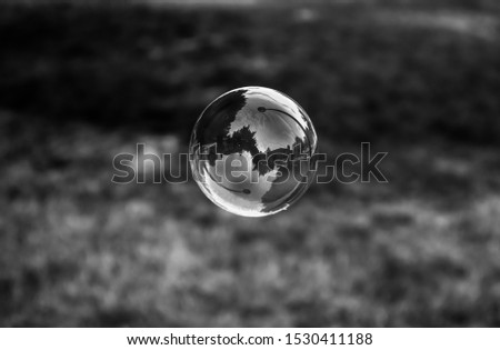 Black and white photo of flying soap bubble with reflection inside it. Parallel world. 