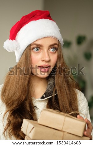 Close-up portrait of a young cute girl in a Christmas hat against the background of the Christmas tree. Christmas and new year concept.
