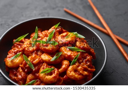 Schezwan Prawns in black bowl at dark slate background. Schezwan Prawns is indo-chinese cuisine curry dish with prawns or shrimps roasted in Schezwan Sauce. Royalty-Free Stock Photo #1530435335