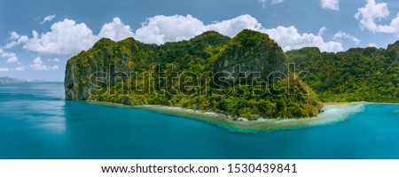 Aerial panoramic drone view of uninhabited tropical island with towering mountains and rainforest jungle surrounded by blue ocean Royalty-Free Stock Photo #1530439841