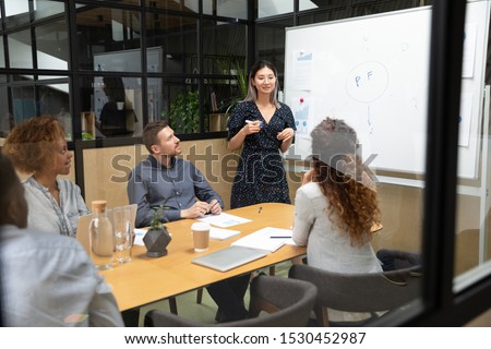 Asian coach speak to staff holding marker use flip chart for visual content at educational seminar, people gathered in boardroom solving issues planning work, cooperation and workshop activity concept