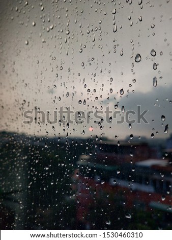 Abstract image of Rain drops on the dirty glass windows with modern office building background. Rain drops on window glasses surface with cloudy background. Big drops of rain on the window glass,