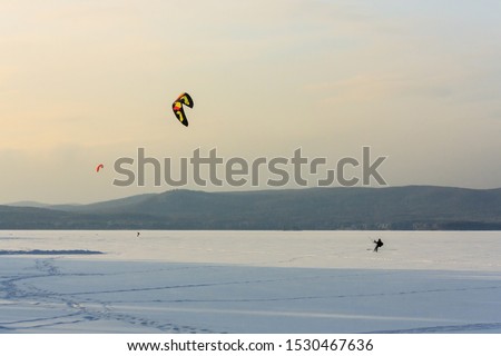 snowkiting the athlete in equipment controls the kite and extreme snowboarding on a huge mountain lake. fresh clean snow and frosty landscape. wild nature background Royalty-Free Stock Photo #1530467636