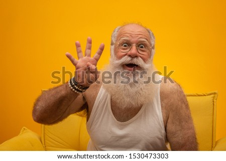 Smiling senior with a long white beard man making four times sign gesture with hand fingers on yellow background. Positive emotion facial expression feelings, attitude, symbol, countdown.