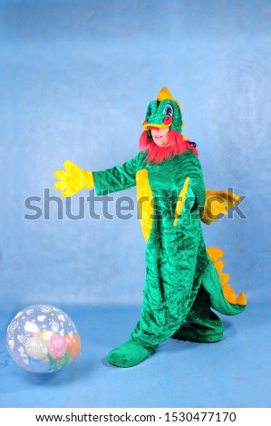 Animator in a green dragon costume with a yellow belly with a ball in the Studio on a blue background