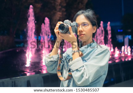 girl photographer In the jean coat take picture at the night with Vintage Film camera .Behind is a fountain.