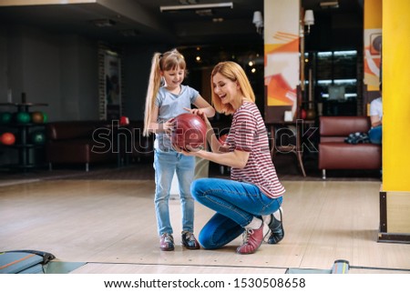 Woman and her little daughter playing bowling in club