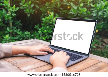 Mockup image of a woman using and typing on laptop with blank white desktop screen on wooden table 