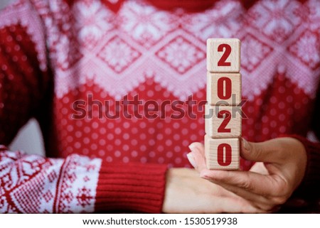 2020 new year concept: wooden cubes in wooman's hands in red winter sweater on background