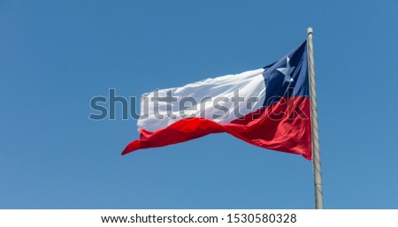 Flag of Chile flies in a strong wind against a bright blue sky with sun glare. Patriotic symbol of Chile, South America.